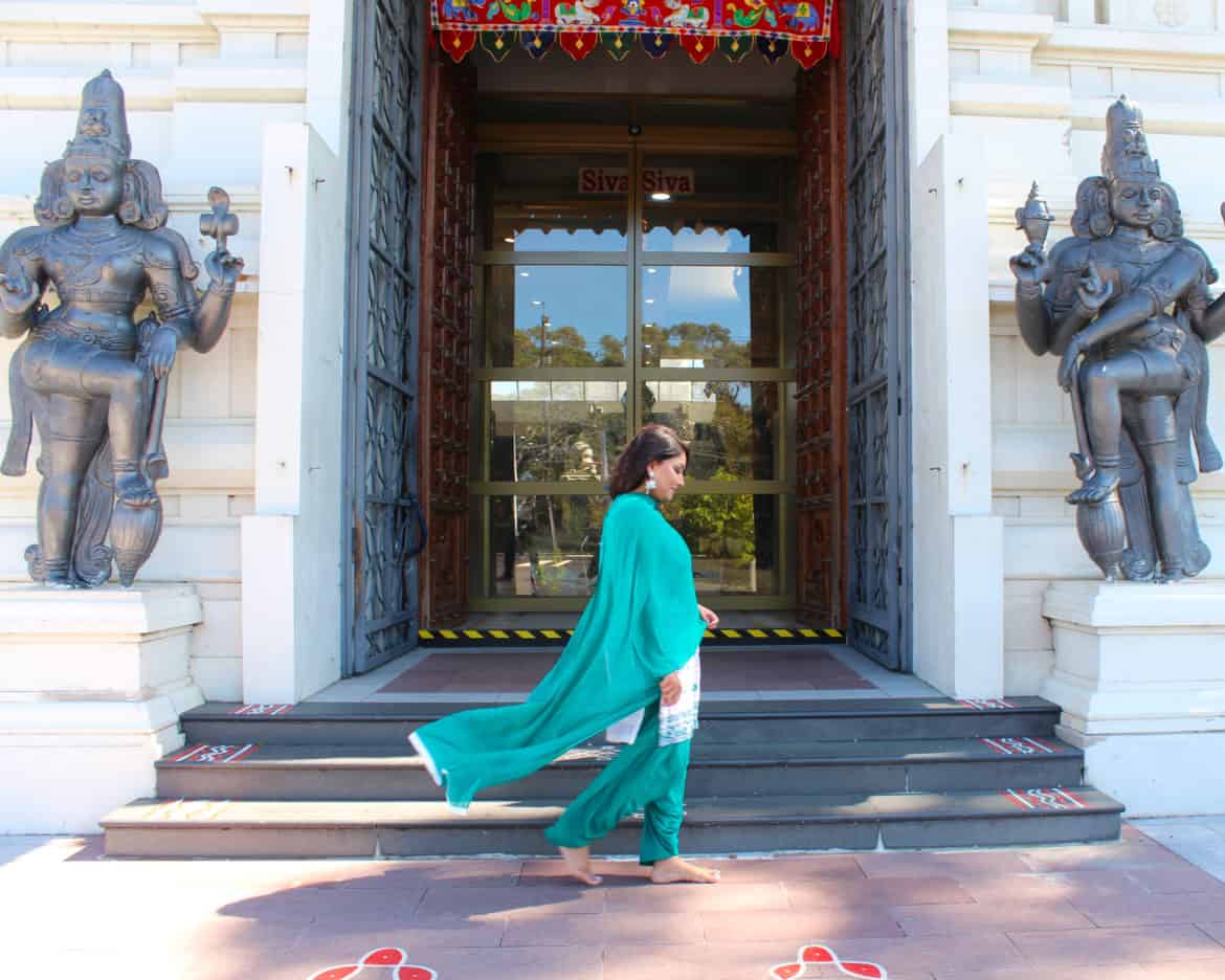 A woman wearing a green sari walking past the temple entrance.